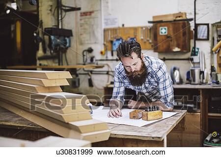 Stock Photo - Mid adult craftsman looking down at blueprint in organ workshop. Fotosearch