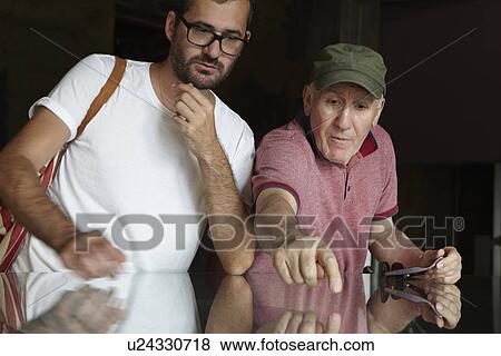 Stock Photo - Mid adult man looking at senior man pointing. Fotosearch
