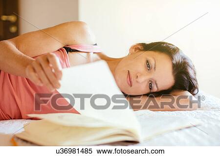 Stock Photography - Mid adult woman lying on bed browsing notebook. Fotosearch