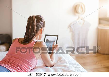 Mid adult woman lying on bed looking at digital tablet View Large Photo Image Stock Photo - Mid adult woman lying on bed looking at digital tablet. Fotosearch