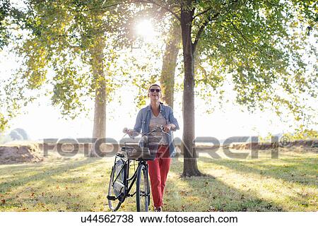 Stock Photo - Mid adult woman pushing bicycle in field, Tuscany, Italy. Fotosearch