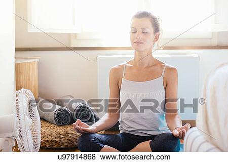 Stock Photo - Mid adult woman sitting on bedroom floor in yoga lotus position. Fotosearch
