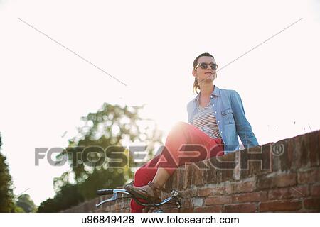 Stock Photo - Mid adult woman sitting on brick wall, Tuscany, Italy. Fotosearch