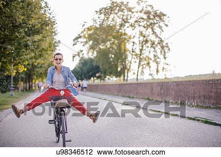 Stock Image - Mid adult woman with legs outstretched on bicycle, Tuscany, Italy. Fotosearch