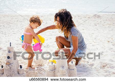 Picture - Mother and toddler daughter building sandcastle on beach, Tuscany, Italy. Fotosearch