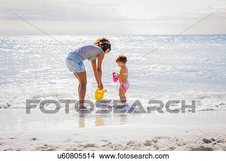 Picture - Mother and toddler daughter collecting water from sea, Tuscany, Italy. Fotosearch