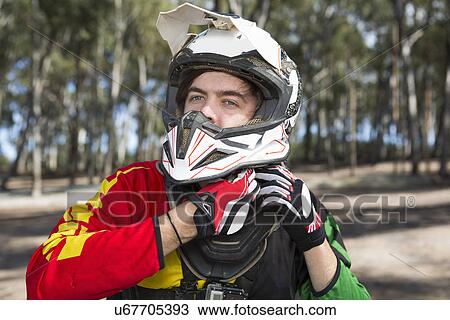 Stock Image - Motocross motorcycle competitor fastening helmet in forest. Fotosearch