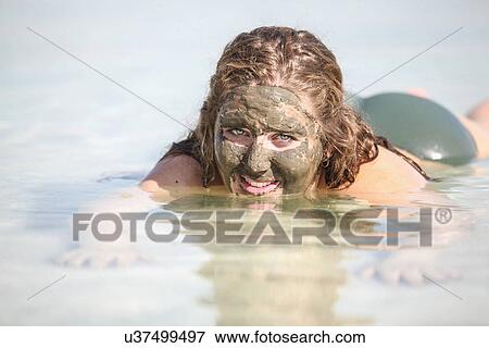 Stock Photo - Mud covered female tourist floats in the Dead Sea, Israel. Fotosearch