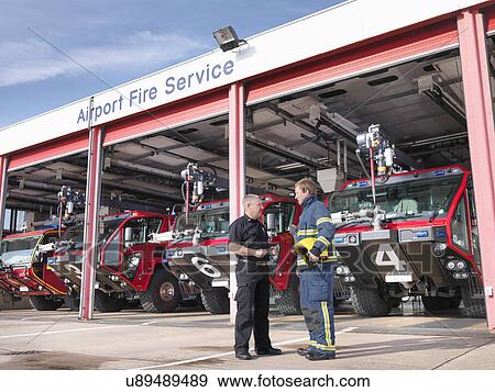 Officer and fireman in front of fire engines in airport fire station View Large Photo Image Stock Photo - Officer and fireman in front of fire engines in airport fire station. Fotosearch