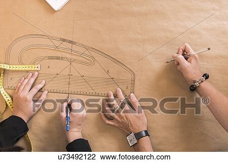 Overhead view of seamstresses hands drawing with curved ruler on dressmakers pattern in workshop View Large Photo Image Stock Image - Overhead view of seamstresses hands drawing with curved ruler on dressmakers pattern in workshop. Fotosearch