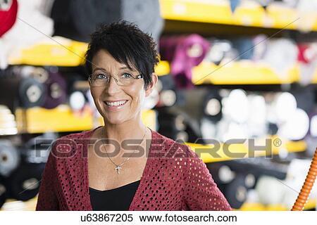 Stock Photography - Portrait of mature seamstress in front of textile shelves in workshop. Fotosearch