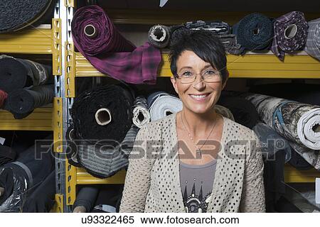 Stock Photography - Portrait of mature seamstress in front of rolls of textile in workshop. Fotosearch