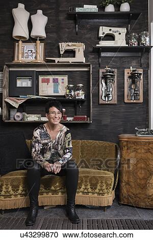 Stock Image - Portrait of mature seamstress sitting in quirky reception at workshop. Fotosearch
