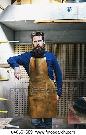 Stock Photo - Portrait of mid adult craftsman leaning on shelf in organ workshop. Fotosearch