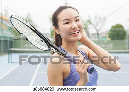 Stock Image - Portrait of young female tennis player on tennis court. Fotosearch