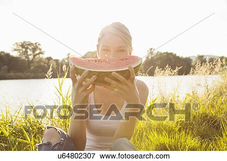 Portrait of young woman holding up melon slice in front of face, Danube Island, Vienna, Austria View Large Photo Image Stock Photo - Portrait of young woman holding up melon slice in front of face, Danube Island, Vienna, Austria. Fotosearch