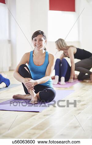 Stock Image - Portrait of young woman sitting on floor in pilates class. Fotosearch