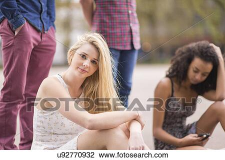 Stock Image - Portrait of young woman with friends in park. Fotosearch