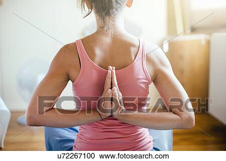 Stock Image - Rear view of mid adult woman in yoga position on bedroom floor. Fotosearch