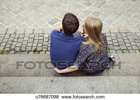 Stock Photo - Rear view of young couple sitting on street sidewalk. Fotosearch