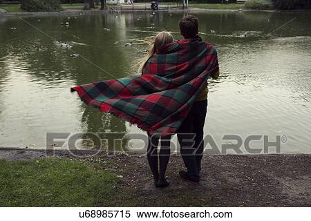 Rear view of young couple wrapped in blanket on park lakeside View Large Photo Image Stock Photography - Rear view of young couple wrapped in blanket on park lakeside. Fotosearch