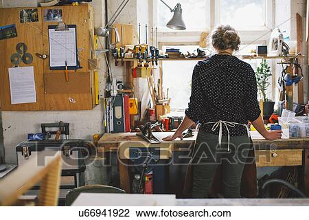 Stock Image - Rear view of young craftswoman at workbench in pipe organ workshop. Fotosearch