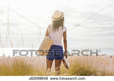 Stock Photo - Rear view of young woman with beach bag in dunes, Tuscany, Italy. Fotosearch