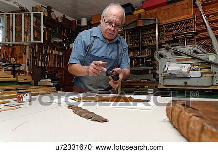 Stock Image - Senior man repairing fragile book spine in traditional bookbinding workshop. Fotosearch