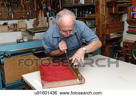 Stock Photograph - Senior man restoring book in traditional bookbinding workshop. Fotosearch