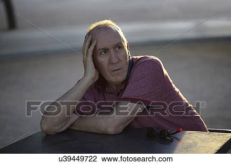 Stock Image - Senior man sitting at table, resting on elbow. Fotosearch