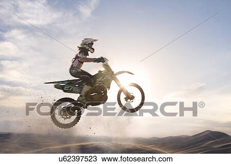 Stock Image - Silhouetted young male motocross racer jumping over mud track. Fotosearch