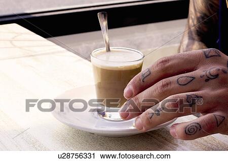 Stock Image - Tattooed hand of young man and coffee shotglass on cafe table. Fotosearch