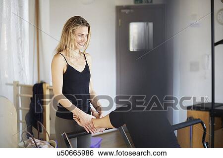 Stock Photograph - Teacher holding feet of female student lying on reformer in pilates gym. Fotosearch