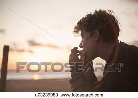 Teenage boy eating snack on beach View Large Photo Image Stock Image - Teenage boy eating snack on beach. Fotosearch