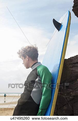 Stock Image - Teenage boy leaning against surfboard. Fotosearch