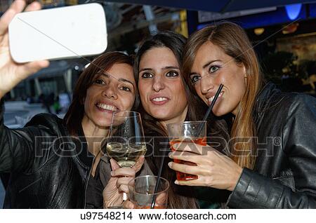Three female friends in bar, taking self portrait using smartphone View Large Photo Image Picture - Three female friends in bar, taking self portrait using smartphone. Fotosearch