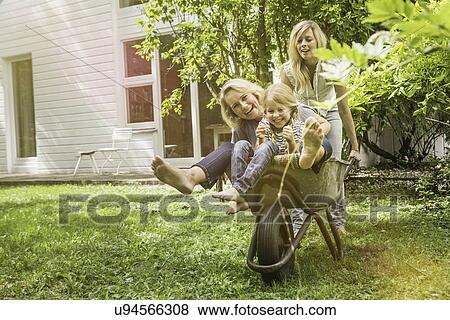 Stock Photo - Three generation of women having fun with wheelbarrow. Fotosearch
