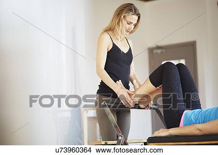 Tutor holding feet of female student lying on reformer in pilates gym View Large Photo Image Picture - Tutor holding feet of female student lying on reformer in pilates gym. Fotosearch