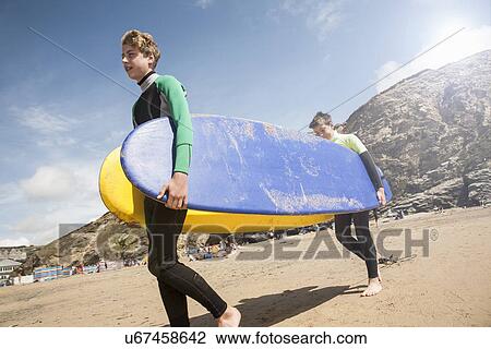 Two boys carrying surfboards on beach View Large Photo Image Stock Image - Two boys carrying surfboards on beach. Fotosearch