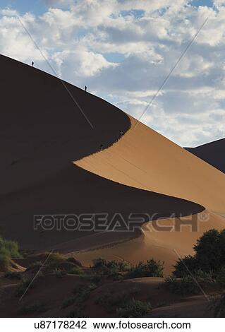 Stock Image - Two people climbing giant sand dune, Sossusvlei National Park, Namibia. Fotosearch