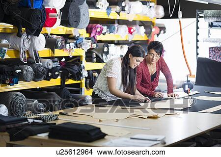 Picture - Two seamstresses chalking design onto textile on work table. Fotosearch