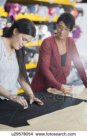 Two seamstresses chalking outline onto textile on work table View Large Photo Image Picture - Two seamstresses chalking outline onto textile on work table. Fotosearch