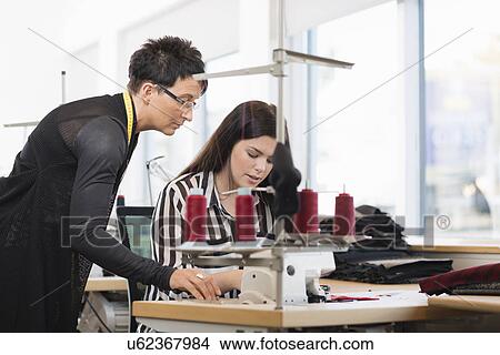 Two seamstresses looking down at sewing machine in workshop View Large Photo Image Picture - Two seamstresses looking down at sewing machine in workshop. Fotosearch