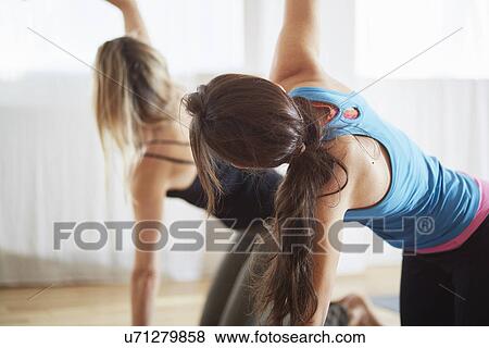Stock Photo - Two women kneeling and raising arms in pilates class. Fotosearch