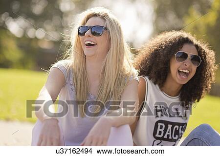 Two young female friends laughing in park View Large Photo Image Picture - Two young female friends laughing in park. Fotosearch