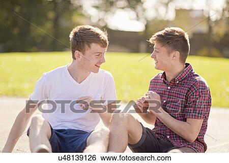 Two young male friends chatting in park View Large Photo Image Stock Photograph - Two young male friends chatting in park. Fotosearch