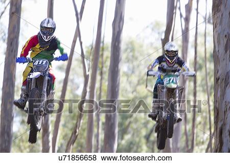 Stock Photo - Two young male motocross riders jumping mid air through forest. Fotosearch