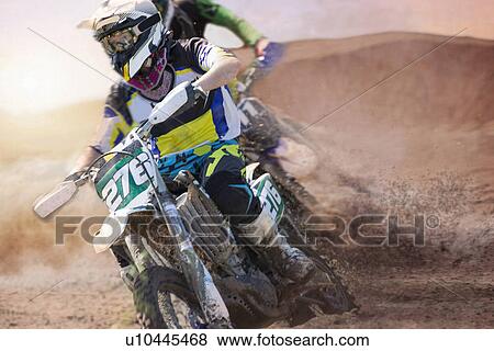 Stock Photo - Two young male motocross riders racing on muddy track. Fotosearch