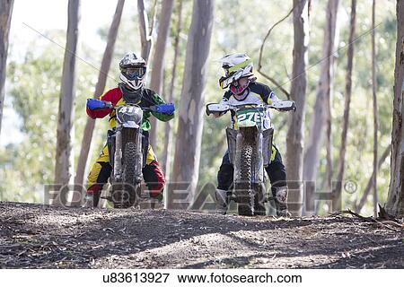 Stock Photo - Two young male motocross riders chatting in forest. Fotosearch