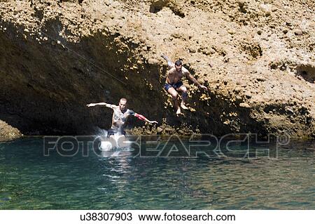 Stock Image - Two young men jumping into sea from rocks, Marseille, France. Fotosearch